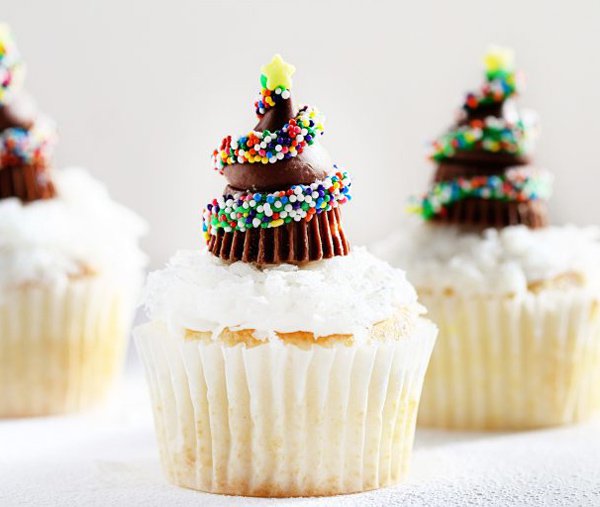 Christmas tree inspired Christmas cupcakes. The vanilla cupcakes are topped with chocolate toppings formed to look like Christmas trees surrounded by colorful candy sprinkles.