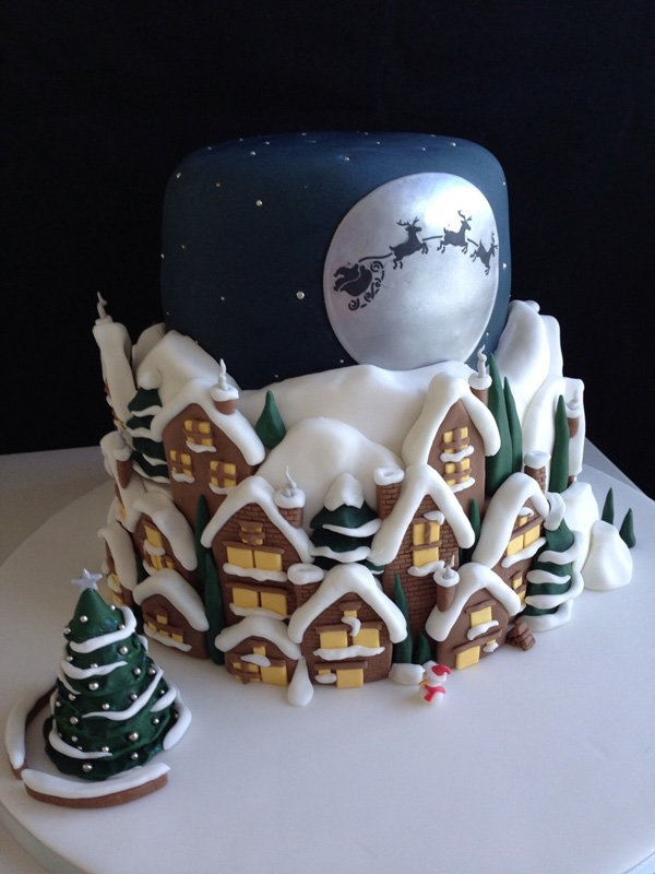 Christmas town inspired Christmas cake. The three layer cake is designed to look like a typical Christmas town at night filled with snow. In the skies you can see the silhouette of Santa riding the sleigh with his reindeer.