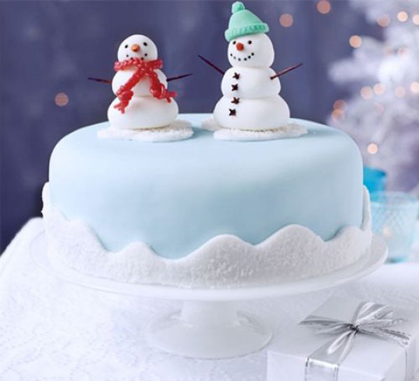 A very cute Christmas cake with a snowman couple on top. The cake is designed to look like a snow yard with two cute snowmen on top that looks like a cute couple under the snow.